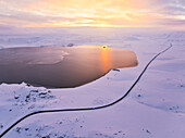 Luftaufnahme einer Drohne von einem Auto, das auf der Straße entlang des Kleifarvatn-Sees fährt, während eines herrlichen Wintersonnenuntergangs, Island, Polarregionen