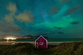 Northern Lights (Aurora Borealis) fill the sky over the red cabin close to Ramberg beach during an autumn night, Lofoten Islands, Nordland, Norway, Scandinavia, Europe