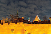 Nächtliche Ansicht der beleuchteten Festungsmauer vor den traditionellen niedrigen Ziegelhäusern und vorbeiziehenden Wolken in der Altstadt von Warschau, Polen, Europa