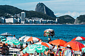 Man selling swimsuits at Copacabana Beach with iconic Sugarloaf mountain in far background, Rio de Janeiro, Brazil, South America