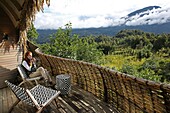 Ruanda, Volcanoes National Park, Frau beim Teetrinken auf der Terrasse einer Suite der Bisate Lodge, einer Lodge der Wilnderness Safaris Hotelgruppe, geöffnet am Mount Bisoke