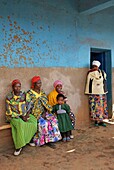 Rwanda, center of the country, villagers in colorful loincloth sitting on a bench in front of a blue wall