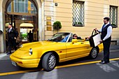 Italy, Lombardy, Milan, Fashion Quadrilateral (Quadrilatero della moda), Alfa Romeo Duetto Spider yellow cabriolet in front of the Four Seasons Hotel Milano, the doorman brings a Gucci bag