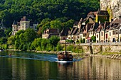 France, Dordogne, La Roque Gageac, Gabare a traditional boat, houses along the Dordogne river and in background the castle of Malartrie