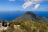 Italien, Sizilien, Äolische Inseln, von der UNESCO zum Weltnaturerbe erklärt, Insel Salina, Wanderer auf dem Gipfel des alten Vulkans Monte Fossa delle Felci mit Blick auf den Zwillingsvulkan Monte dei Porri, im Hintergrund die Inseln Filicudi und Alicudi