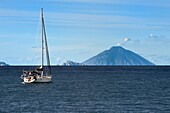 Italien, Sizilien, Äolische Inseln, von der UNESCO zum Weltkulturerbe erklärt, Fähre, die die Inseln verbindet, Segelboot auf dem Weg zur Insel Panarea in der Mitte und der Vulkan Stromboli im Hintergrund