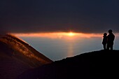 Italien, Sizilien, Äolische Inseln, von der UNESCO zum Weltnaturerbe erklärt, Insel Stromboli, Wanderer beobachten die Fumarolen eines Ausbruchs an den Hängen des aktiven Vulkans bei Sonnenuntergang