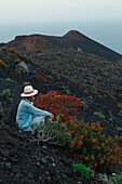 Spain, Canary Islands, La Palma, hiker sitting on the edge of the road, in front of a volcanic landscape