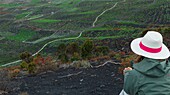 Spain, Canary Islands, La Palma, hiker sitting on the edge of the road, in front of a volcanic landscape