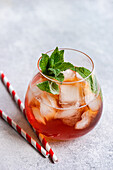 A Coke cocktail filled with ice, garnished with fresh mint leaves, and served with striped straws in a clear glass.