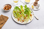 Top view of a classic Caesar salad with crisp romaine lettuce, crunchy croutons, shaved Parmesan cheese, and creamy dressing, served on a white plate presented on a white background.