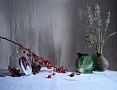 Artistic still life featuring tiny red crab apples, a split radicchio, and a lush savoy cabbage arranged on a textured grey backdrop with subtle lighting.