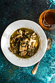 From above traditional Georgian stewed meat with white wine, green plums, tarragon, coriander, parsley, and spring onion, served in a white bowl with a vintage spoon, and a glass of wine.