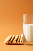 Freshly baked oatmeal cookies aligned beside a full glass of milk on an orange background, inviting a cozy snack time.