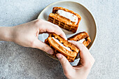 Hands holding delicious homemade waffles with a creamy vanilla marshmallow layer in a casual home setting