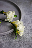 A close-up view of elegant white freesia flowers resting against a gray textured table, suggesting a refined and gentle table setting theme perfect for special occasions