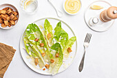 Top view of a Caesar salad with crispy romaine lettuce, croutons, and shaved Parmesan cheese, elegantly plated on a white background.