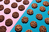 Top view of various chocolate chip and double chocolate cookies symmetrically placed on a contrasting pink and blue surface. The image highlights the texture and deliciousness of these freshly baked treats