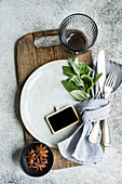 This image captures an aesthetically pleasing summer table setting highlighted by a mint decoration, star anise, featuring a white plate, gray napkin, silver utensils, and a small blackboard