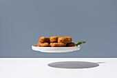 Levitating plate of crispy croquettes garnished with fresh herb on a gray background with shadow below