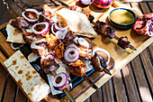 Juicy charcoal-grilled mtsvadi skewers served on a wooden platter, complemented by slices of onion, juicy pomegranate, and traditional Georgian bread, in an authentic setting