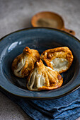 Three freshly cooked Georgian khinkali dumplings, beautifully presented on a deep blue ceramic plate, garnished with an accent of subtle herbs