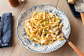 Von oben, hausgemachte italienische Pasta garniert mit frischer Petersilie und geriebenem Parmesan auf einem Holztisch mit Pfeffermühle und Käsereibe