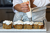 Crop anonymous cook with pastry bag with cream decorating vegan carrot cakes while preparing desserts in bakery