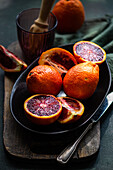 Fresh blood oranges on a dark plate with vibrant red interiors displayed on a rustic wooden board