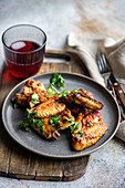 Delicious roasted chicken wings in a spicy sauce garnished with fresh coriander. Served on a grey plate with a cherry cocktail on the side.