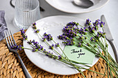 A beautifully arranged summer table setting featuring a white plate adorned with vibrant lavender flowers and a 'Thank you' card, symbolizing elegant hospitality