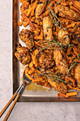 Top view of juicy roasted chicken wings paired with seasoned sweet potatoes on a baking tray garnished with fresh thyme.