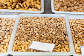 Assorted trays of pistachios on display at a market, with focus on the shelled nuts in the foreground