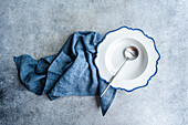 Elegant white plate with blue scalloped edges, a silver spoon, and a blue napkin set on a textured background