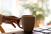 Die Hand einer reifen Frau hält eine Tasse Kaffee.