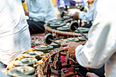 Nahaufnahme der Hände einer unkenntlich gemachten Person, die während einer kulturellen Zeremonie traditionelle thailändische Musikinstrumente spielt und die Kunst der thailändischen Musik vorführt.