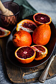 Vibrant blood oranges, some sliced, arranged on a dark rustic plate alongside vintage cutlery, evoking a fresh and natural feel