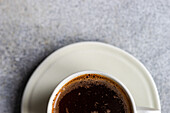 A top view of a freshly brewed hot coffee in a white cup placed on a saucer, with a foamy surface, perfect for a morning energy boost.