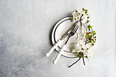 Elegant spring table setting with white blossom branches and vintage-style cutlery on a textured grey background