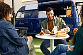 Friends share smiles and a casual meal outside a trendy blue food truck, showcasing an enjoyable urban eating experience