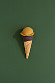 A vibrant pistachio ice cream scoop sits atop a classic waffle cone against a green background, casting a playful shadow