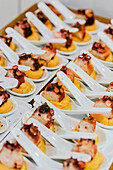 Rows of chic white spoons hold perfectly cooked octopus pieces atop a dollop of sauce, ready for a high-end gastronomic event