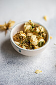 A delicate arrangement of dried roses in a ceramic bowl, placed on a textured grey surface, capturing a serene and vintage aesthetic