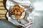 A freshly baked sourdough loaf made with rye flour, resting on a wooden board covered with a white kitchen towel