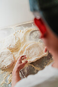 An over-the-shoulder view of a pizza chef stretching dough in a pizzeria, with a faceless and cropped portrayal focusing on the hands and dough