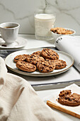 A serene table setting with a cup of espresso, a glass of milk, and chocolate chip cookies on a plate, accompanied by a cozy book