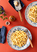 From above, Alfredo pasta dinner with creamy white sauce and herbs served on a red table with pepper mill , parmesan grater and a blue napkin