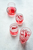 Top view of elegant glasses filled with a refreshing cherry vodka and tonic cocktail, accompanied by ice cubes, set on a textured surface.