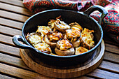 A tantalizing skillet full of baked mushroom caps generously topped with golden, melted Sulguni cheese, served on a wooden table, providing a rustic and appetizing visual