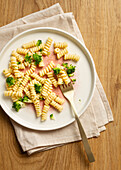 Eleganter gesprenkelter Teller mit einer Portion Fusilli-Nudeln mit Brokkoliröschen, dazu eine goldene Gabel auf einer beigen Serviette und einem hölzernen Hintergrund